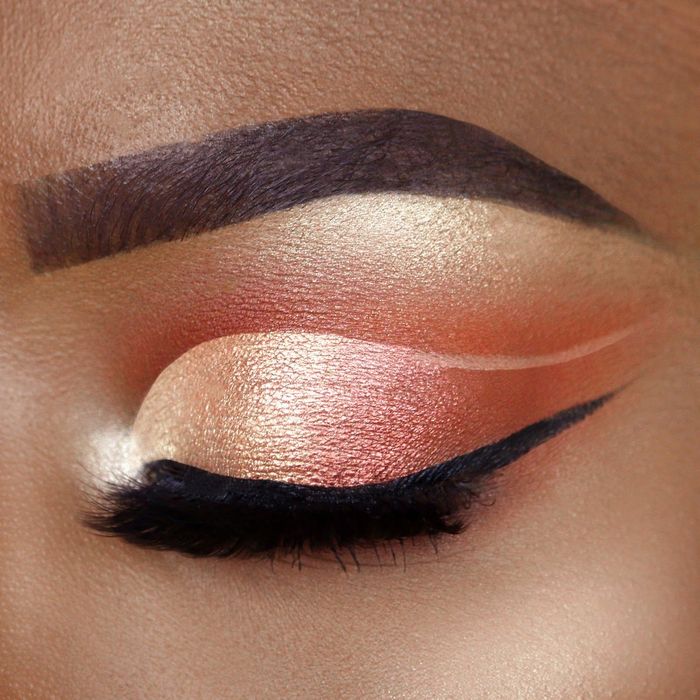 A close-up view of an eye with vibrant orange and gold eyeshadow, dramatic winged eyeliner, and mascara for a striking look