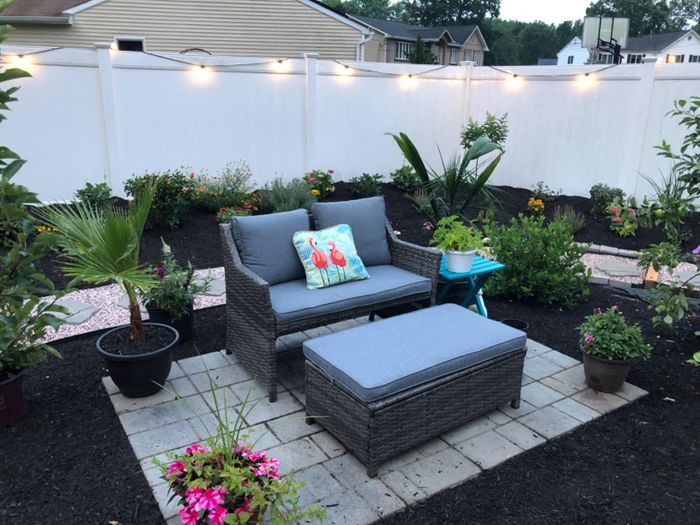 A patio furniture set with cushions and a side table, set in a garden adorned with hanging lights