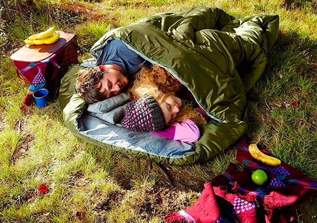 Two individuals snuggling up in a large sleeping bag, side by side