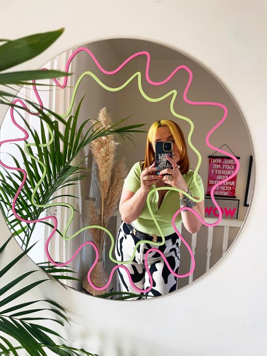 model posing in a circular mirror with a green and pink squiggly design