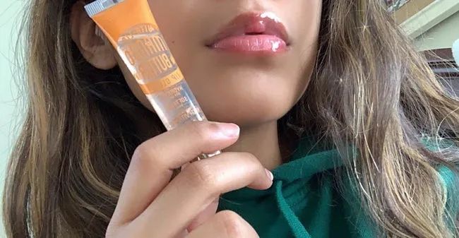 A reviewer shows off their glossy lips while holding the lip gloss