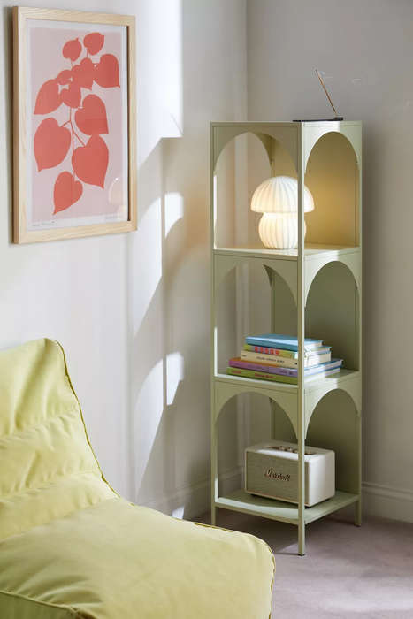 A modern arched shelving unit with books and decorative items, placed next to a green chair