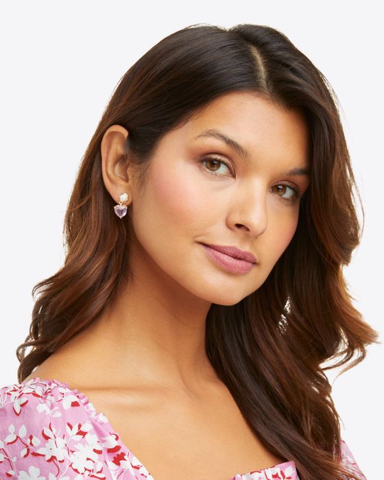 A model wearing pink heart-shaped dangling earrings with a pearl post