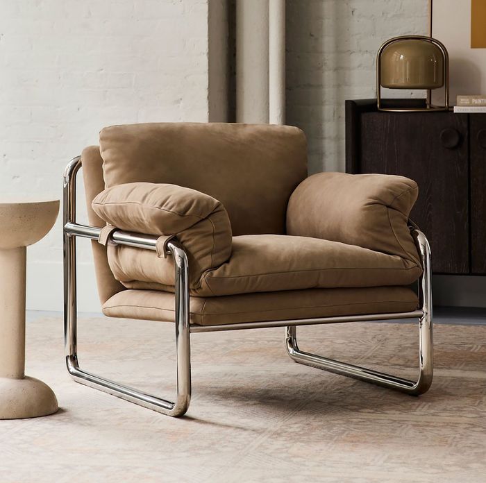 A modern beige cushioned armchair with a sleek chrome frame, placed in a trendy interior setting