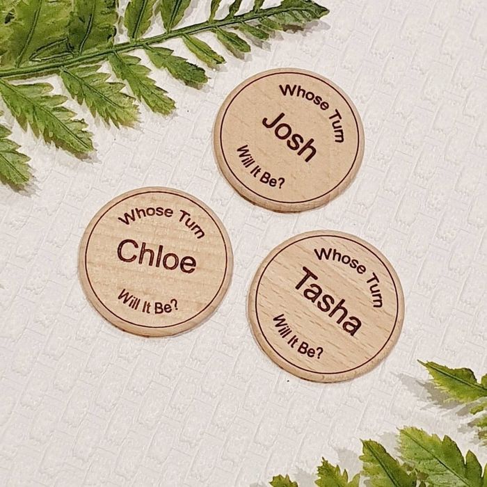 Three wooden coins, each engraved with 'whose turn will it be?' and a name in the center.