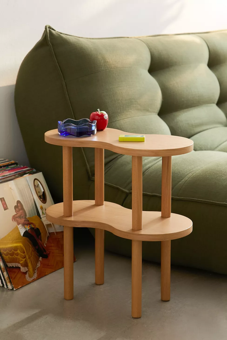 A modern two-tier wooden side table with decorative items placed on top, positioned next to a green couch