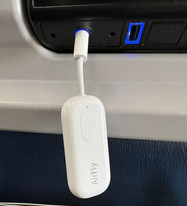 A review photo showing the AirFly Pro plugged into the headphone jack at the back of an airplane seat.