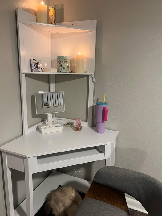 Cozy white desk adorned with candles, a few decorative accents, a hydration bottle, and a fluffy pet tucked beneath it