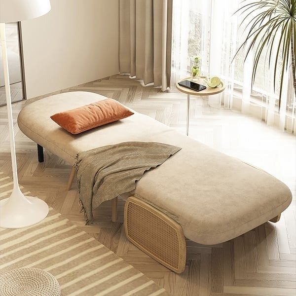 A modern chaise lounge with a cozy pillow and throw blanket, placed in a sunlit room filled with plants and tasteful decor