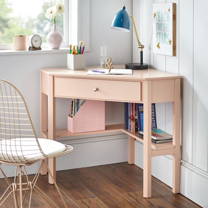 Compact desk with a drawer, a stack of books, a pink organizer, and a blue lamp. A motivational quote on the wall reads,