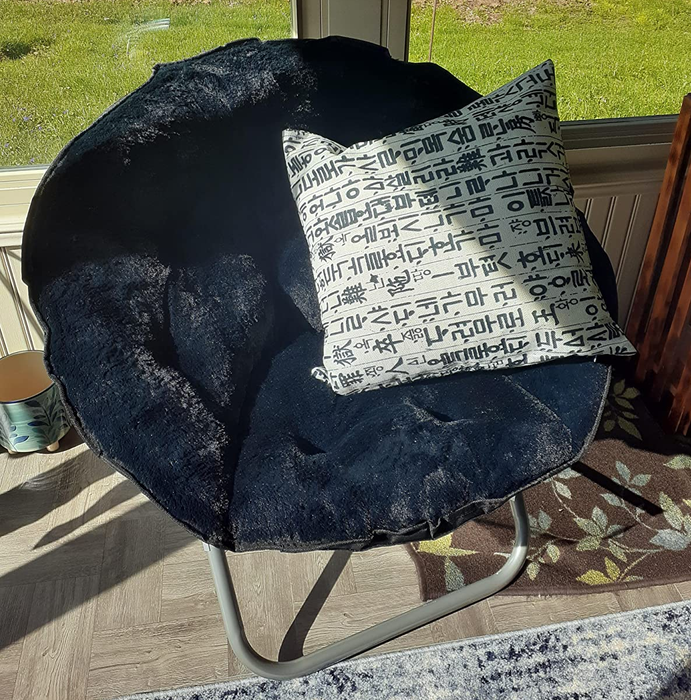 A reviewer's image showcasing a black saucer chair adorned with a black and white throw pillow.