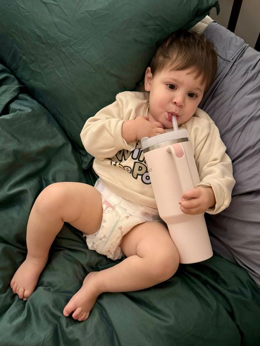 A toddler sipping from a rose quartz Stanley tumbler.