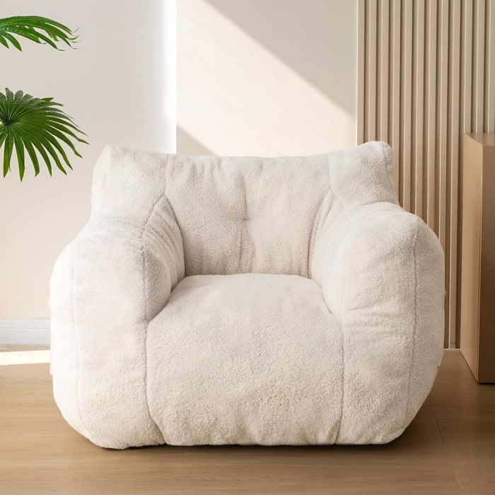A large, soft white armchair with a textured fabric, placed in a minimalist space with wooden floors and a small potted plant.