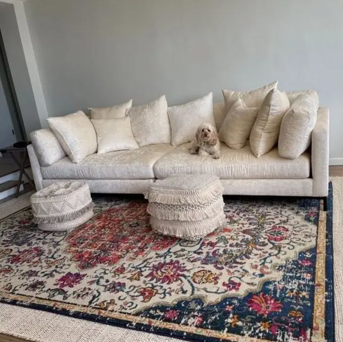 oversized light beige velvet sofa adorned with many pillows and a dog lounging on top, complete with ottomans