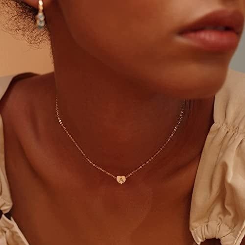 A model wearing a delicate chain with a gold heart pendant featuring an 'a' inside