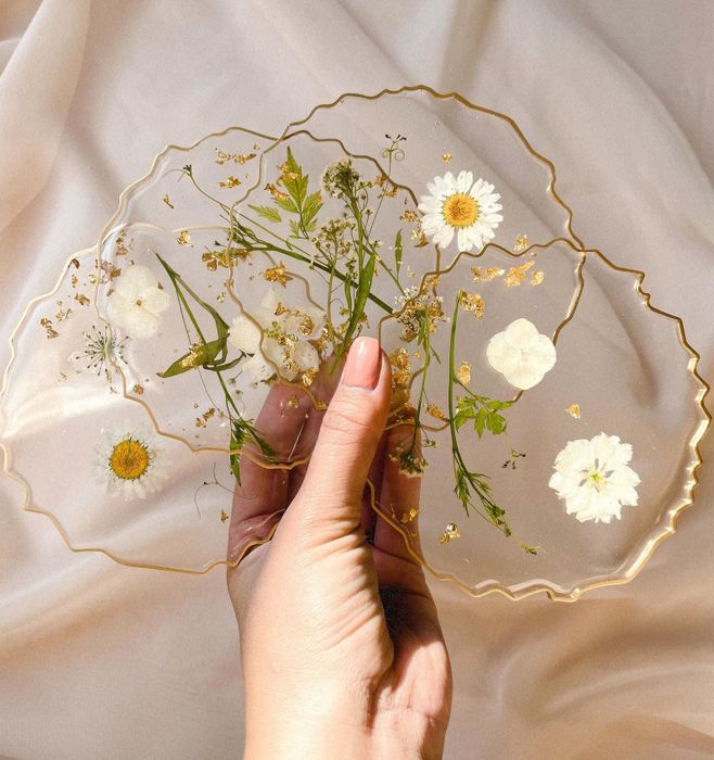 Set of clear coasters with uneven gold rims and delicate white pressed flowers trapped inside.