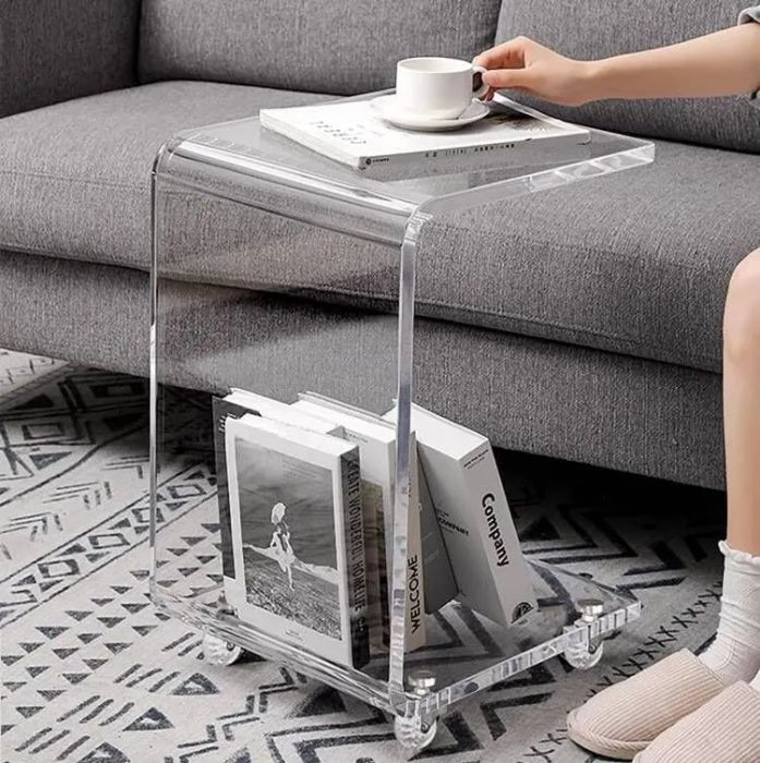 A clear acrylic C-shaped coffee table with four wheels for mobility.