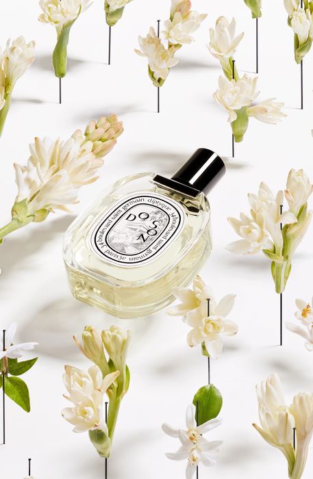 A Diptyque perfume bottle nestled in a bed of vibrant flowers.