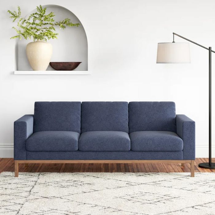 blue three-seater sofa with wooden base next to a floor lamp