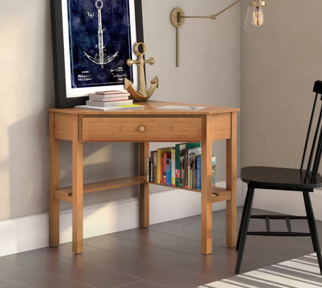 a light wood corner desk in a room, with books arranged on the bottom shelf
