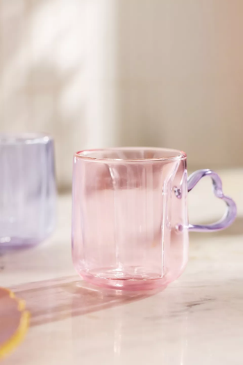 A pink glass mug featuring a heart-shaped purple handle.
