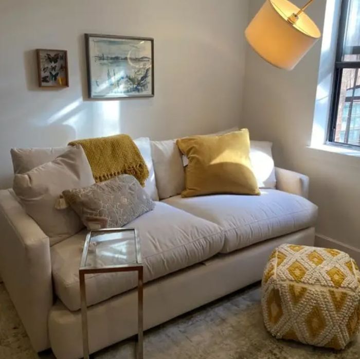 small white two-seat sofa in a living room setting, adorned with yellow throw pillows
