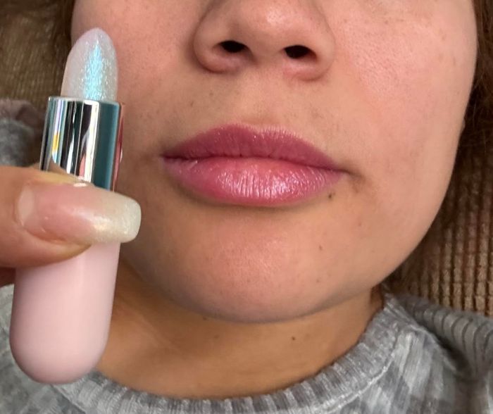 A reviewer holding a sparkly lip balm and showcasing their pink, shimmery lips.
