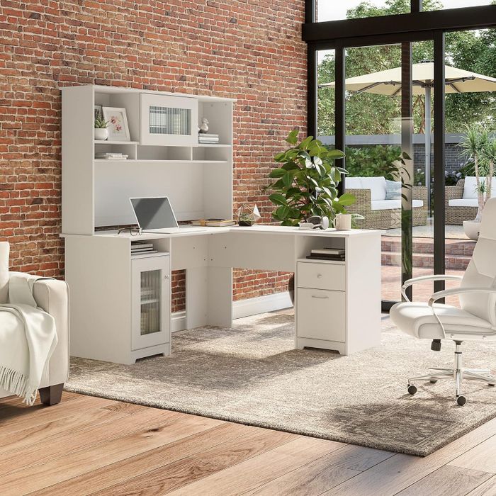 A modern L-shaped desk with shelves and a laptop, placed in a bright home office space