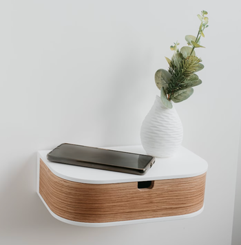 A minimalist floating shelf with a vase filled with greenery and a smartphone placed on it, suggesting chic decor choices