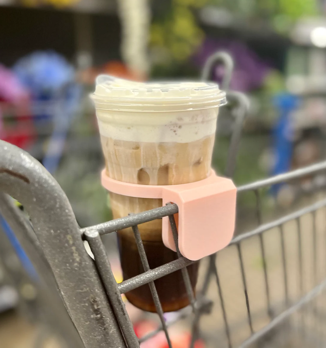 A pink, 3D-printed drink holder that clips onto the side of a shopping cart for easy beverage access while you shop.