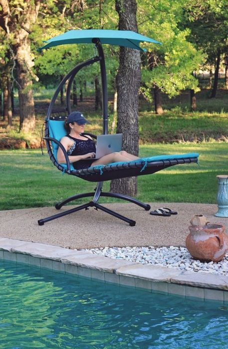 A reviewer comfortably relaxing in a blue swing while working on their laptop.