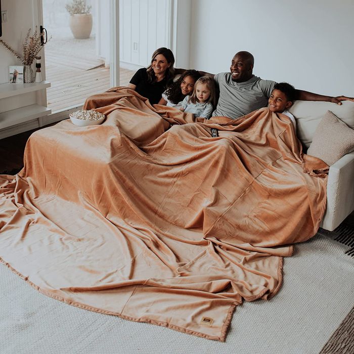 A group of two adults and three children enjoying the warmth of a spacious tan blanket.