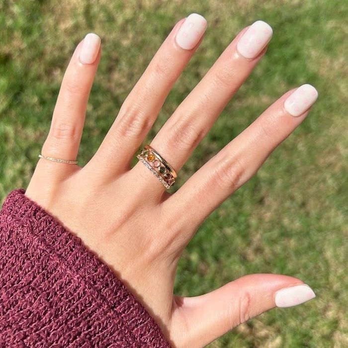 A model wearing white press-on nails adorned with tiny pink hearts.