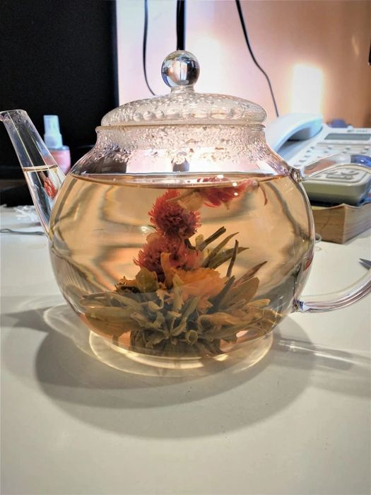 A reviewer's photograph showing the glass teapot with blooming tea flowers unfolding inside, creating a visually stunning moment.