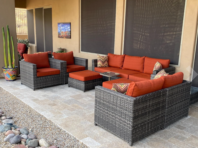 A cozy patio arrangement featuring a brown wicker outdoor furniture set with vibrant red cushions, complete with a corner sectional sofa, two armchairs, and a compact coffee table
