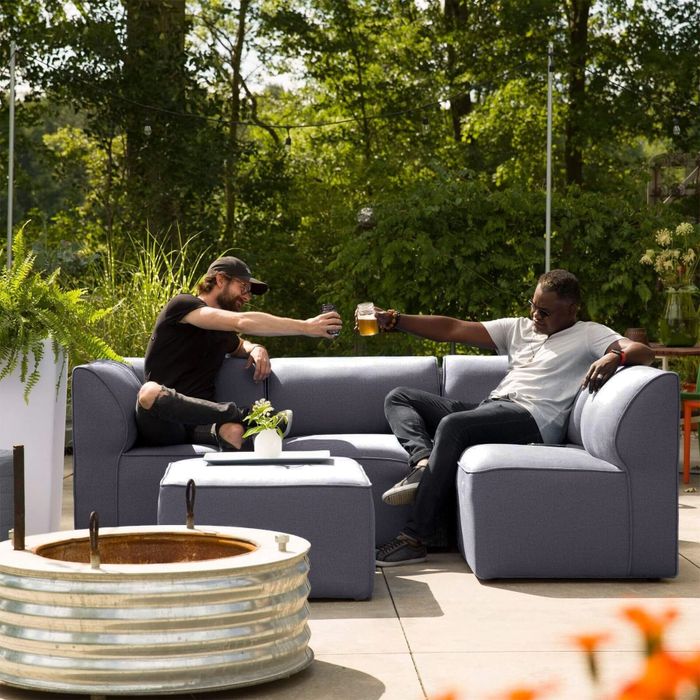 Two individuals seated on a modern outdoor sofa, toasting with glasses in a beautifully landscaped garden, highlighting stylish patio furniture.