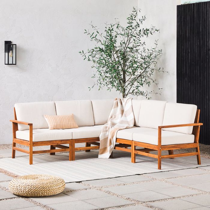 A contemporary outdoor sectional sofa on a patio, adorned with white cushions and a striped throw blanket, positioned beside a lush plant