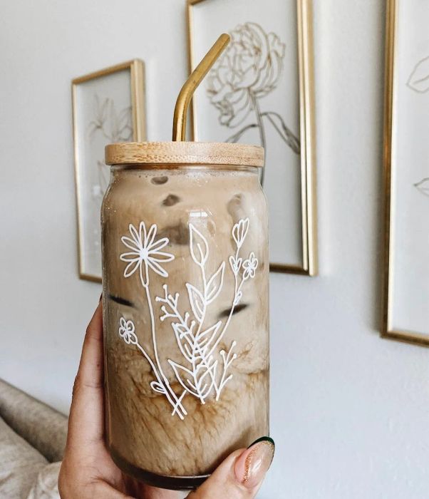 A hand holding the iced coffee glass adorned with a floral design.