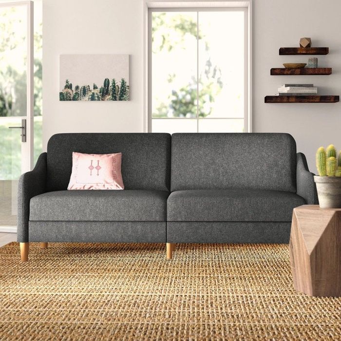 A contemporary living room showcasing a grey loveseat, a jute rug, wooden shelves, a geometric wooden coffee table, framed artwork, and potted plants