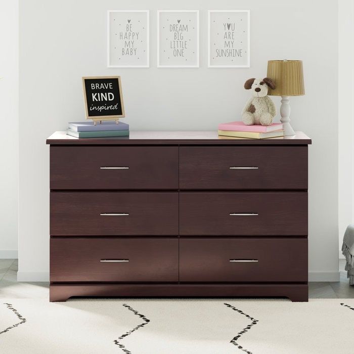 A wooden six-drawer dresser, topped with books, a lamp, and a stuffed animal. Three motivational wall prints hang above for inspiration.