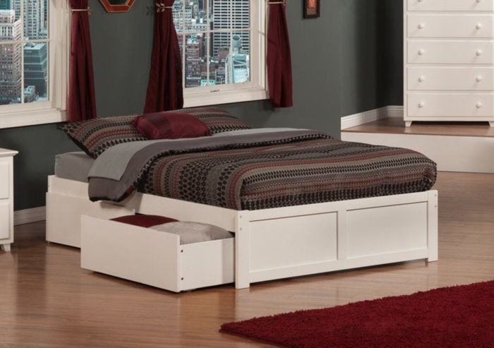 A contemporary bedroom setup featuring a white bed frame with storage drawers beneath, coordinating bedding, and a matching dresser and nightstand, all framed by a stunning city view.