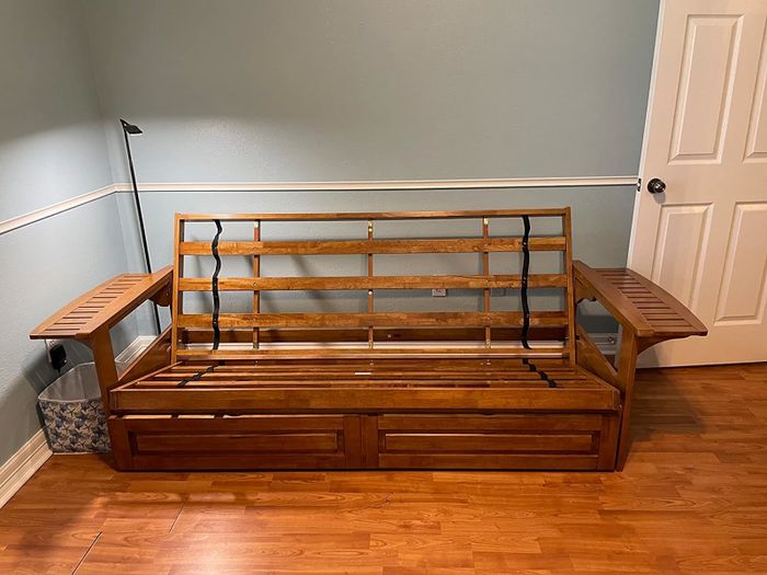 A wooden futon frame with side trays in a room, easily converting into a bed. A great option for small spaces.