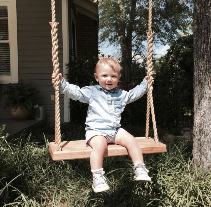 A toddler peacefully sitting on a tree swing.