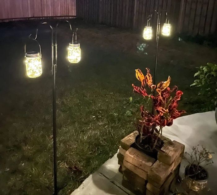A reviewer’s photo of the lanterns hanging from hooks on stakes in a backyard, glowing softly in the evening.