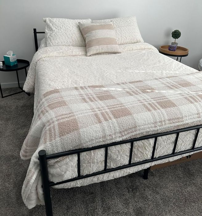 A neatly arranged bed with a decorative comforter set, accompanied by a small bedside table featuring a plant.