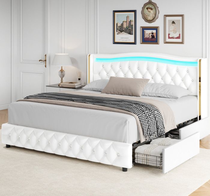 A contemporary bedroom featuring a white tufted bed frame with built-in storage drawers. The headboard is illuminated and upholstered, set against a backdrop of framed artwork.