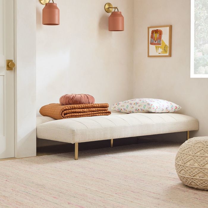 A stylish minimalist room showcasing a beige daybed adorned with decorative pillows and a cozy knit pouf, ideal for a chic modern setting.