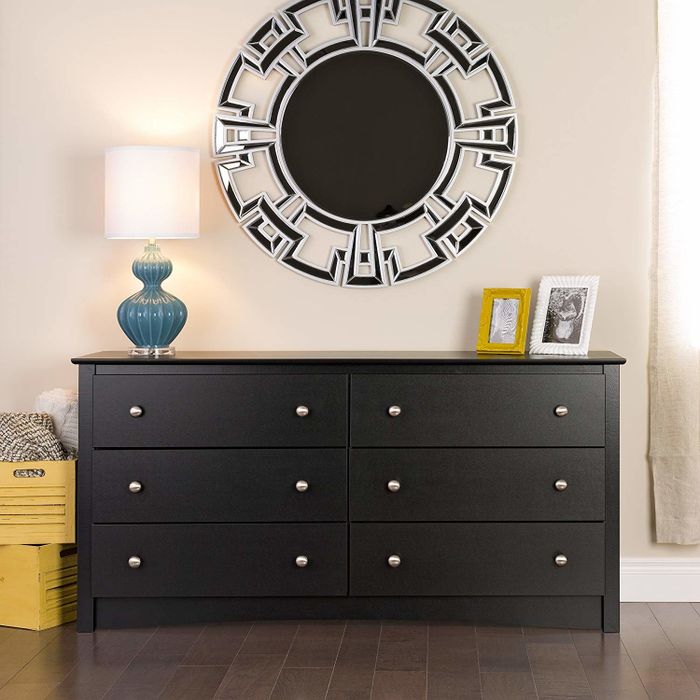 A modern six-drawer dresser with a decorative mirror, a table lamp, and framed photos on top. Yellow storage boxes sit beside it for added style.