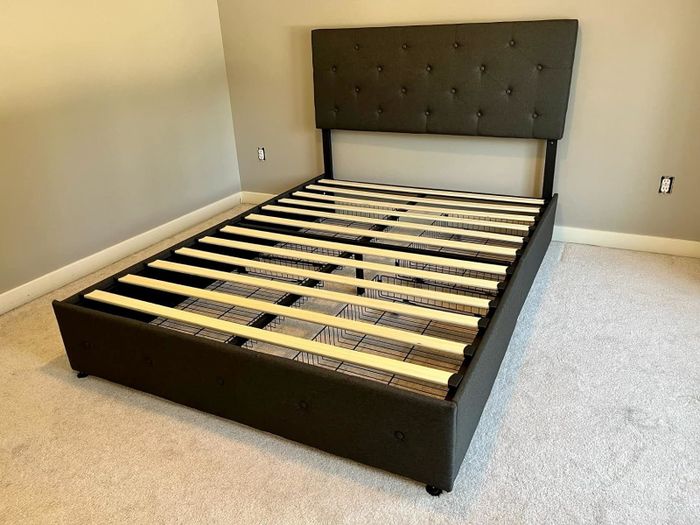An unmade queen-sized bed frame with a tufted headboard, set in a minimalist room.