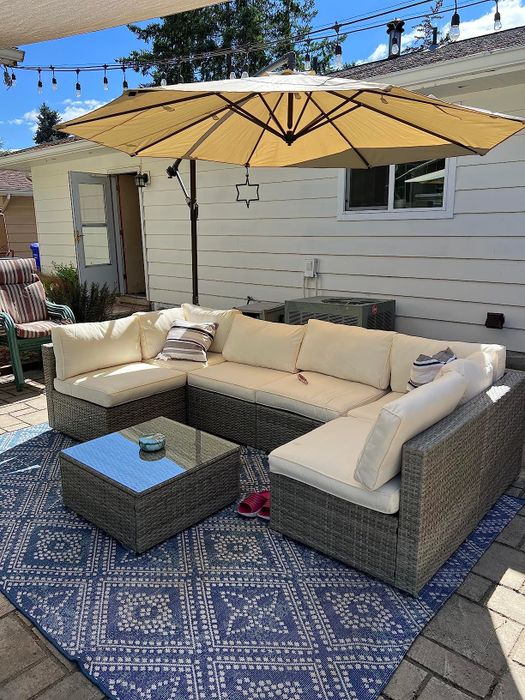 A reviewer's photo showcasing a cream U-shaped sectional surrounding a glass-top coffee table, with an umbrella overhead offering shade.